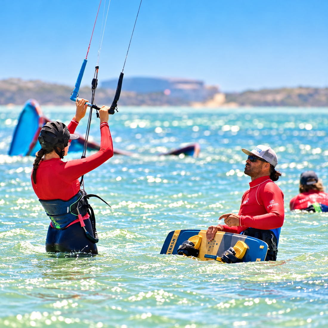 Beginner kitesurfing student flying a kite in shallow water on Langebaan Lagoon while an instructor holds the board